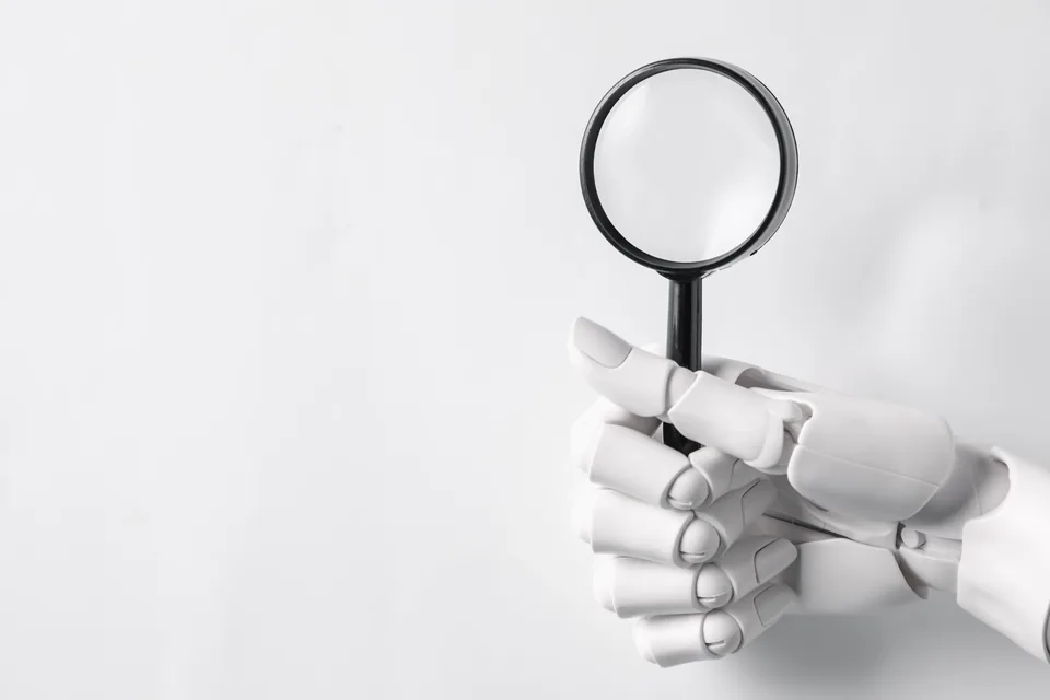 Robotyczna dłoń trzymająca lupę na jasnym tle jako symbol audytu SEO