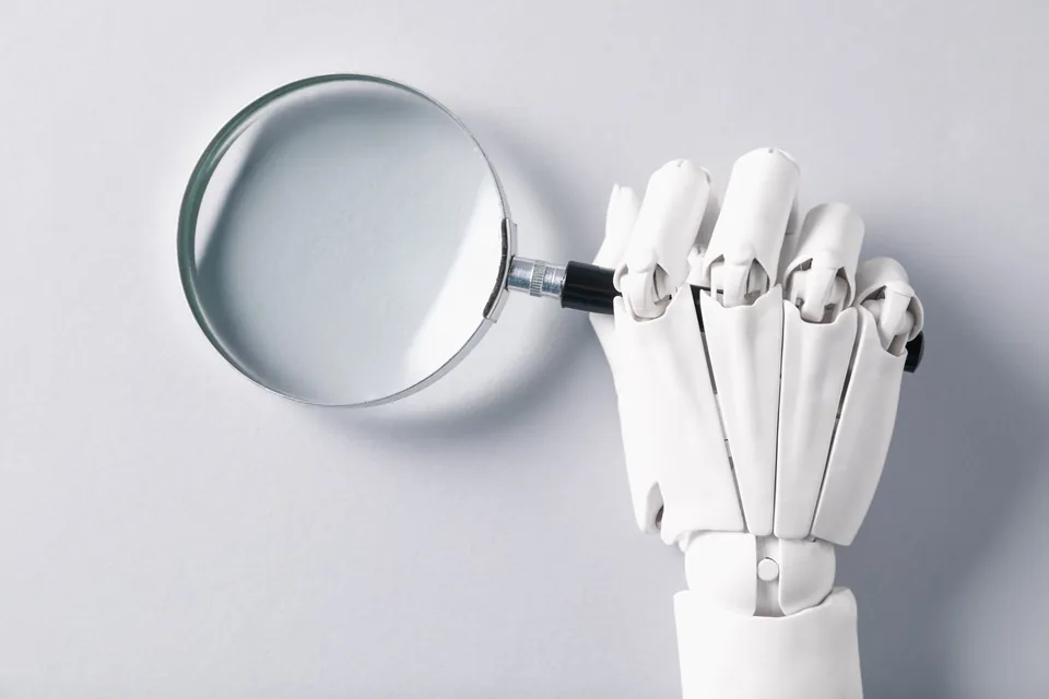 Robotyczna dłoń trzymająca lupę jako metafora wyszukiwania przez AI